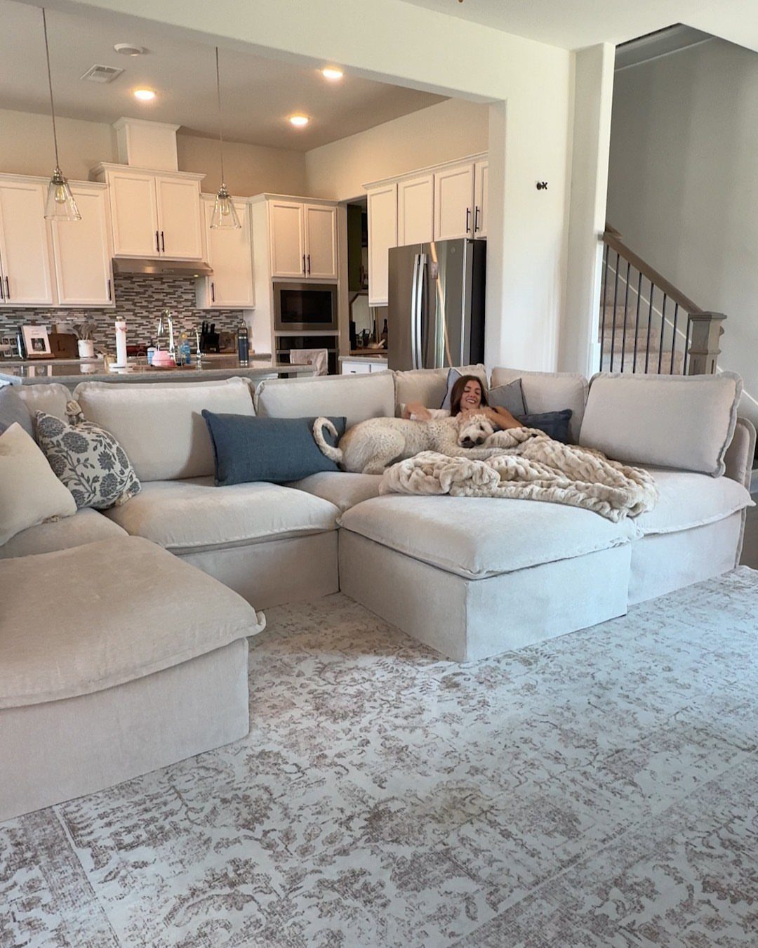 Beige sectional sofa with a white fluffy blanket and patterned grey area rug.
