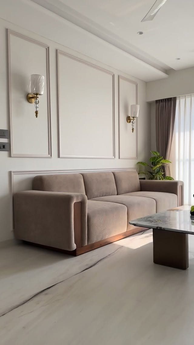 Beige fabric sofa in a living room with white paneled walls and grey curtains.