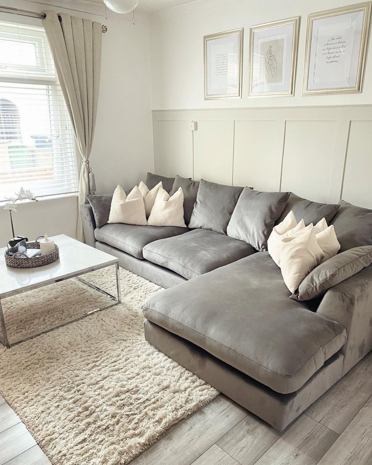 Grey velvet sectional sofa with beige pillows in a room with beige walls.