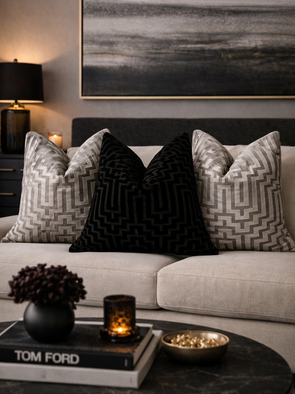 Beige sofa with grey geometric and black velvet layered throw pillows in a living room.