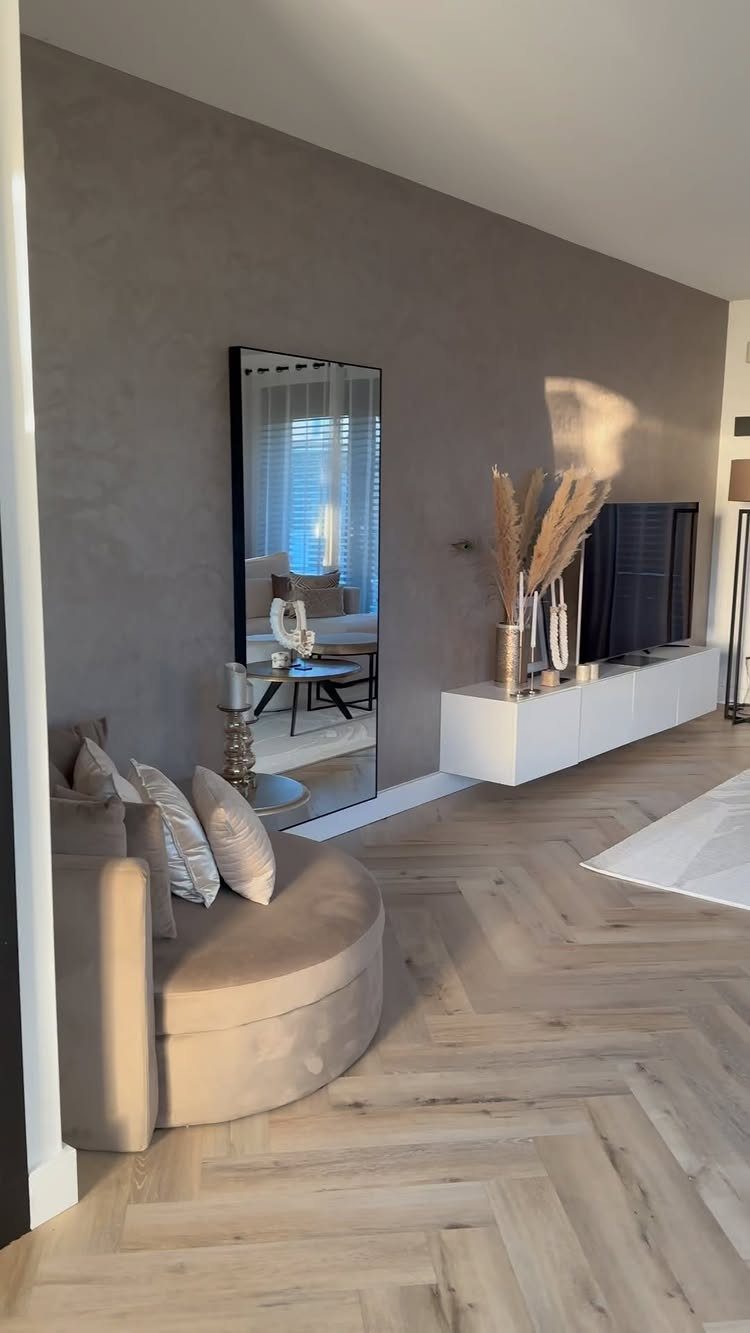 Modern living room with grey walls, beige curved sofa, and herringbone wood flooring.