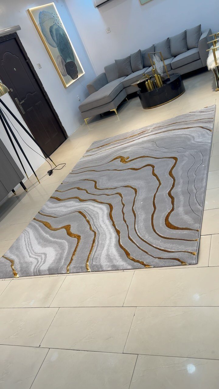 Grey rug with wavy beige patterns on a light beige tiled living room floor.