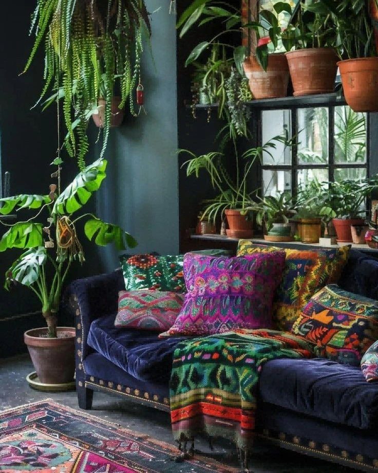 Navy velvet sofa with colorful pillows against a dark accent wall with many plants.