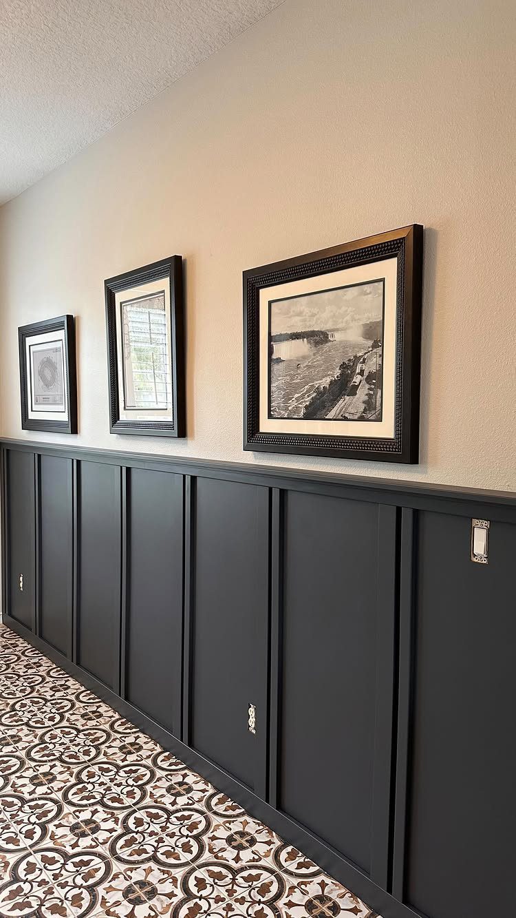 Dark grey wainscoting paneling on a beige wall with framed art and patterned tiles.
