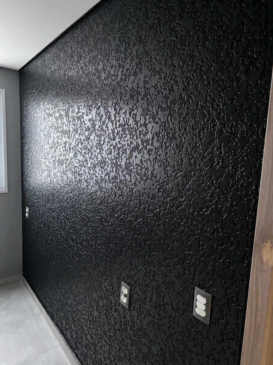 Textured black wall with a stippled finish and electrical outlets in a room.