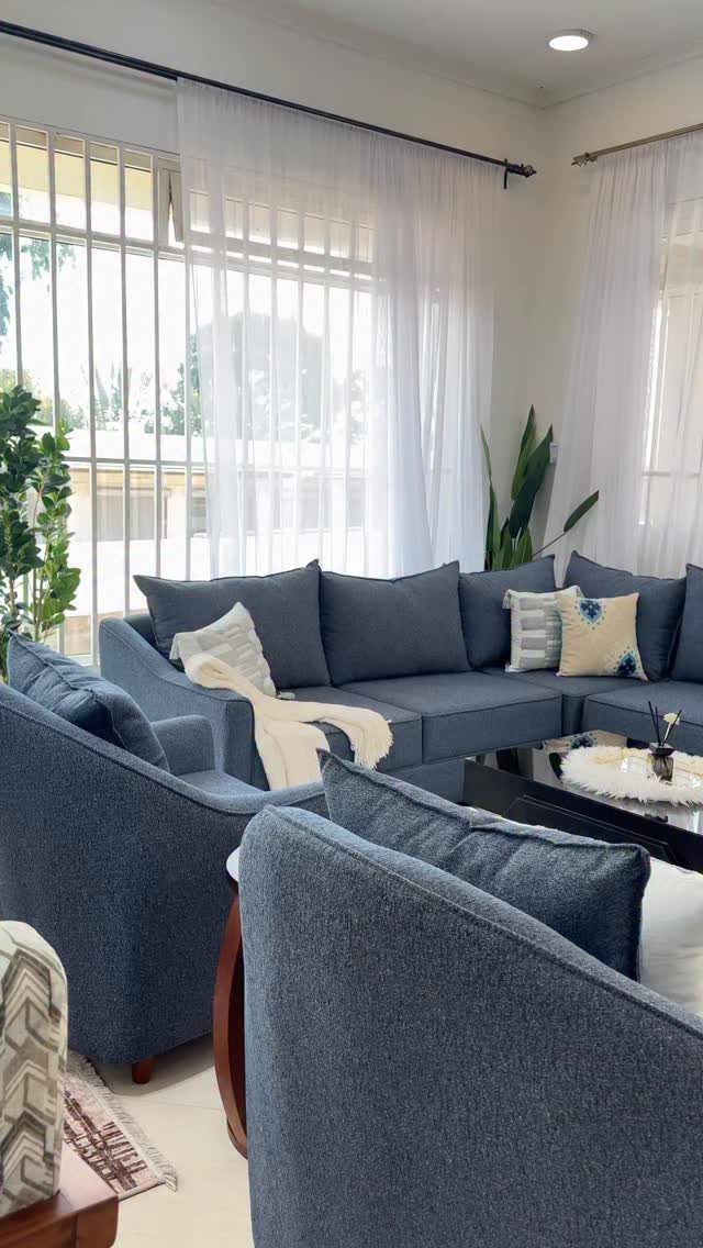 Blue sectional sofa and armchairs in a bright living room with white curtains.