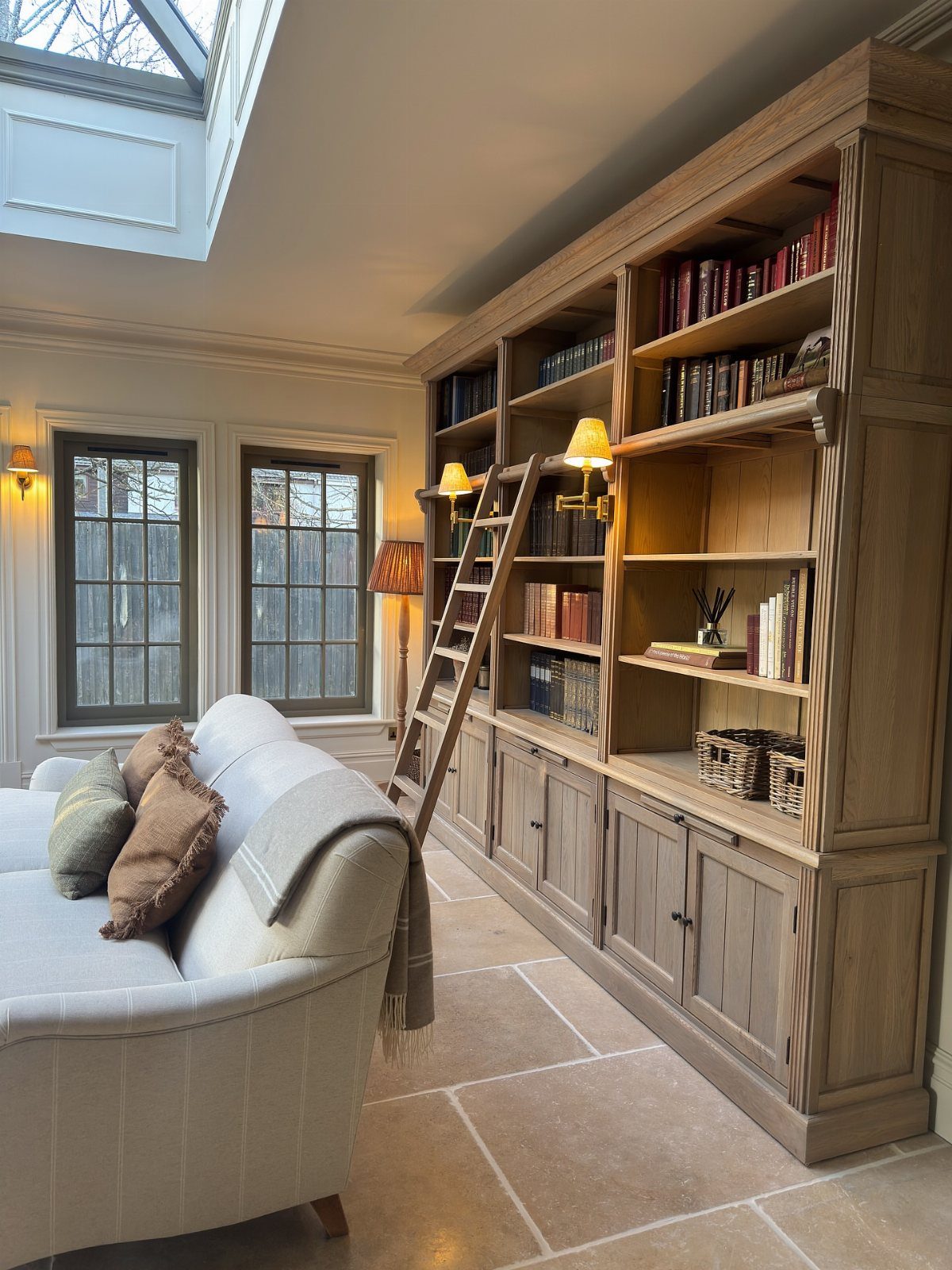 Large light-wood built-in bookshelf with a rolling ladder in a bright living room