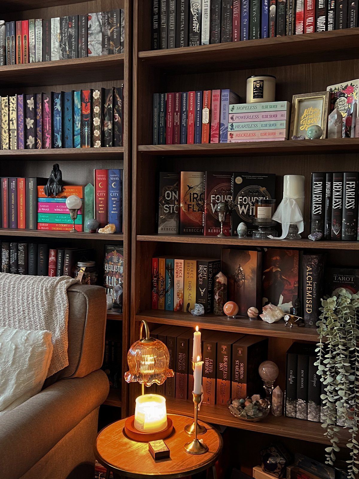 Dark wood bookshelves filled with books, crystals, and candles next to a cozy sofa.