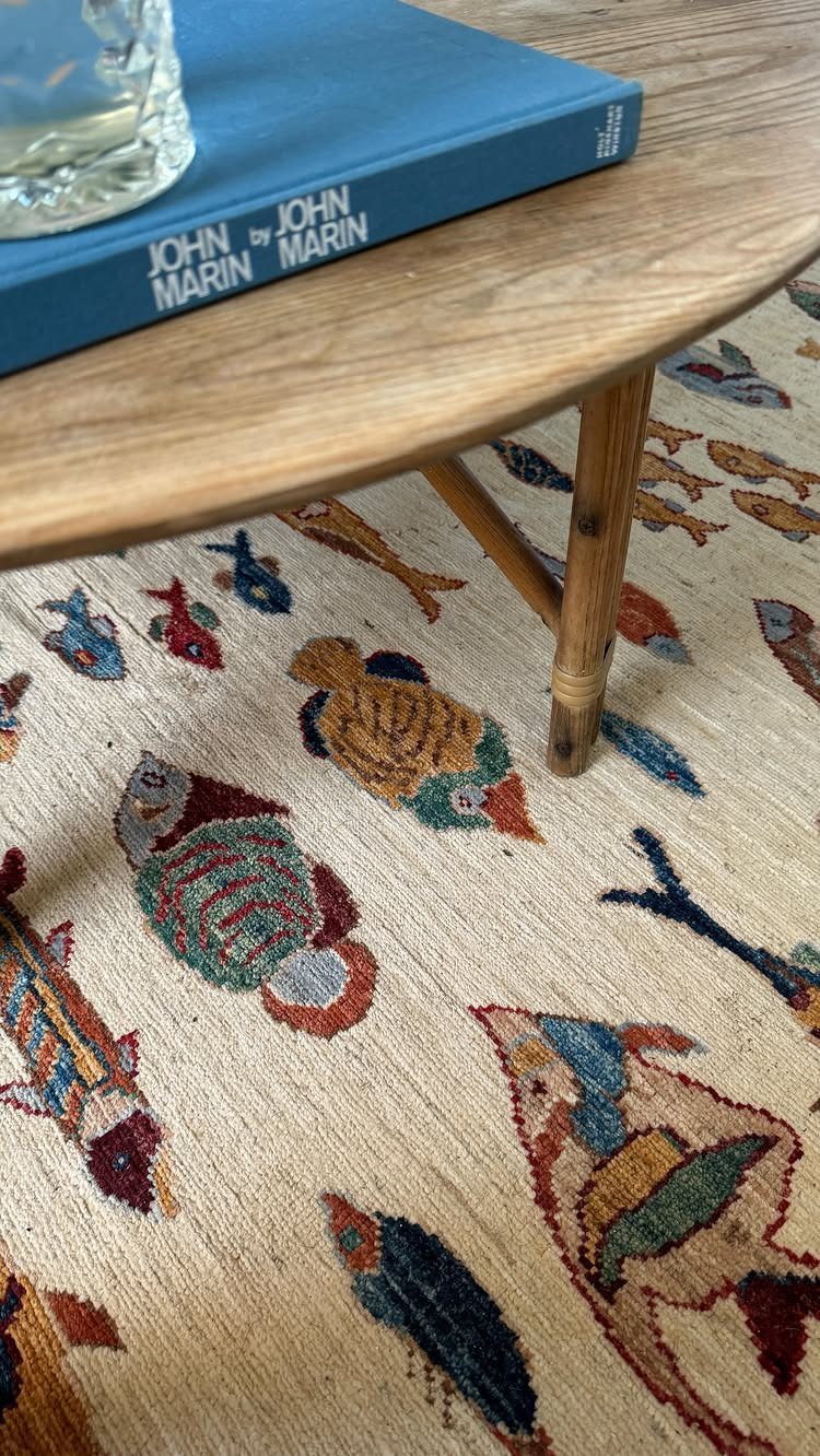Cream rug with colorful fish patterns under a wooden coffee table and blue book.