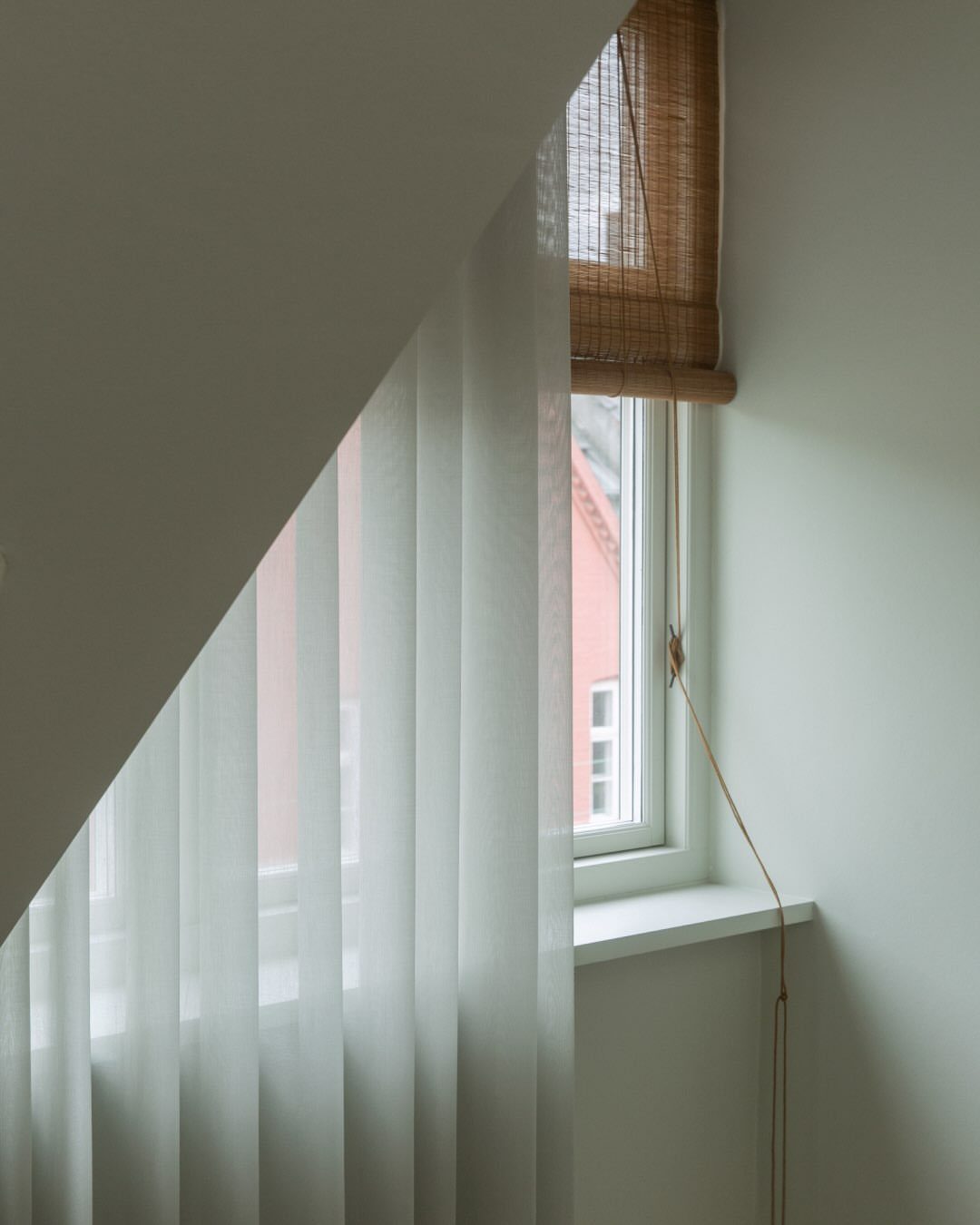 White sheer curtains and a bamboo blind hanging by a bright window.