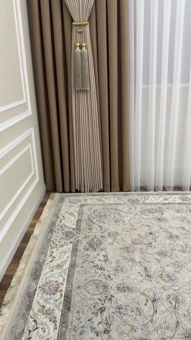 Brown and white curtains with gold tiebacks above a patterned beige area rug.
