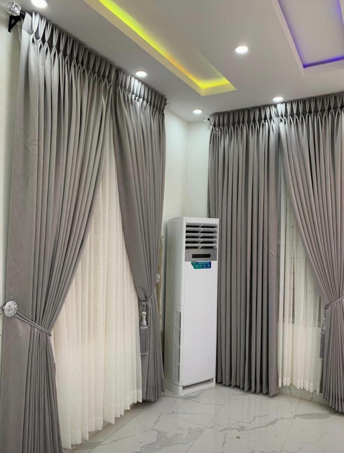 Grey floor-to-ceiling drapery panels with white sheer curtains in a modern living room.