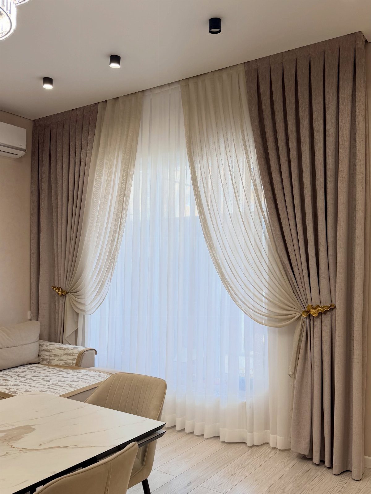 Taupe drapery panels with gold tie-backs layered over white sheer curtains in a room.