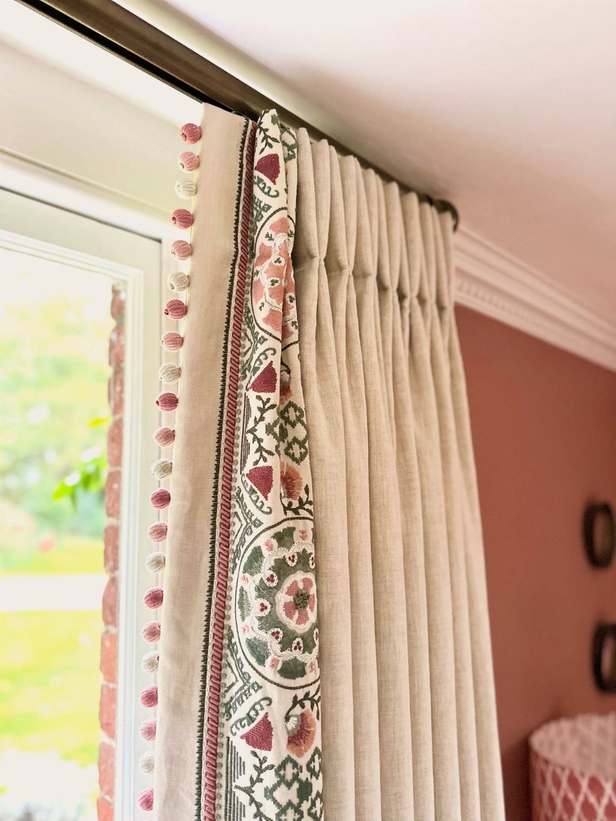 Floral patterned curtains with pom-pom trim paired with neutral beige pleated drapery panels.