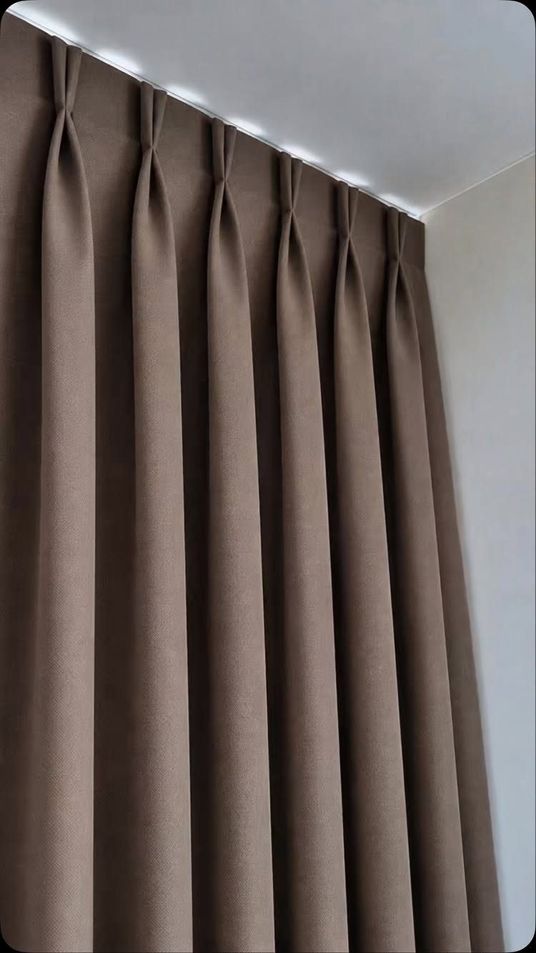 Brown pleated curtains hanging from a ceiling track with integrated white LED lighting.