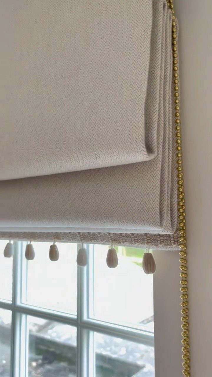 Beige fabric Roman blind with tassel trim and gold beaded pull cord.