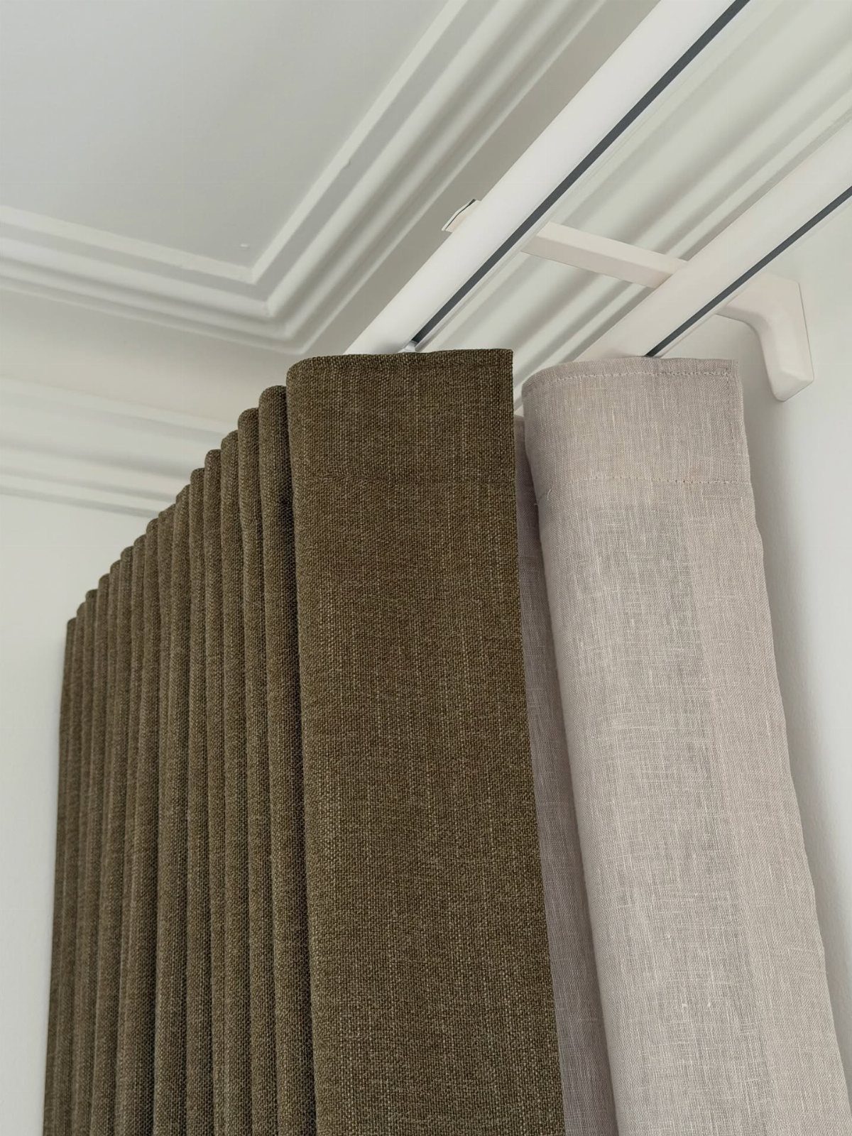 Olive brown and beige textured fabric curtains hanging from a white ceiling track.