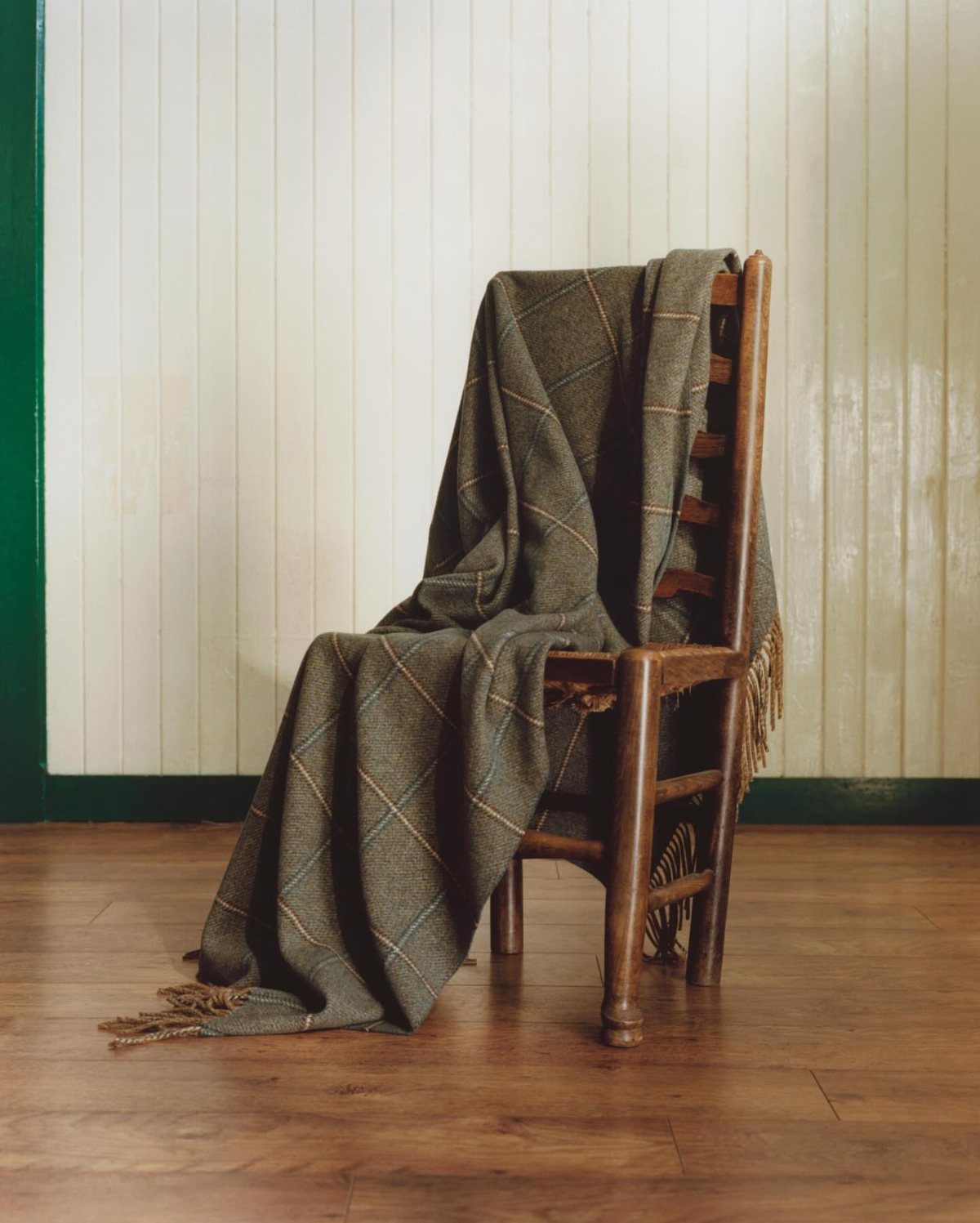 Plaid tartan throw blanket draped over a wooden chair on a hardwood floor.