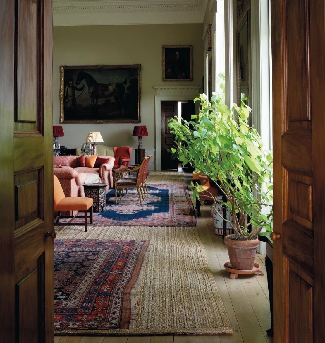 Layered Persian and jute rugs on a wooden floor in a traditional living room.