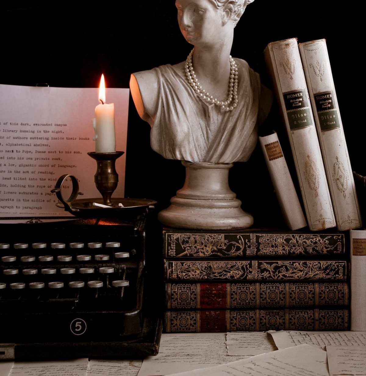 Leather-bound books stacked next to a vintage typewriter and a classical white bust.