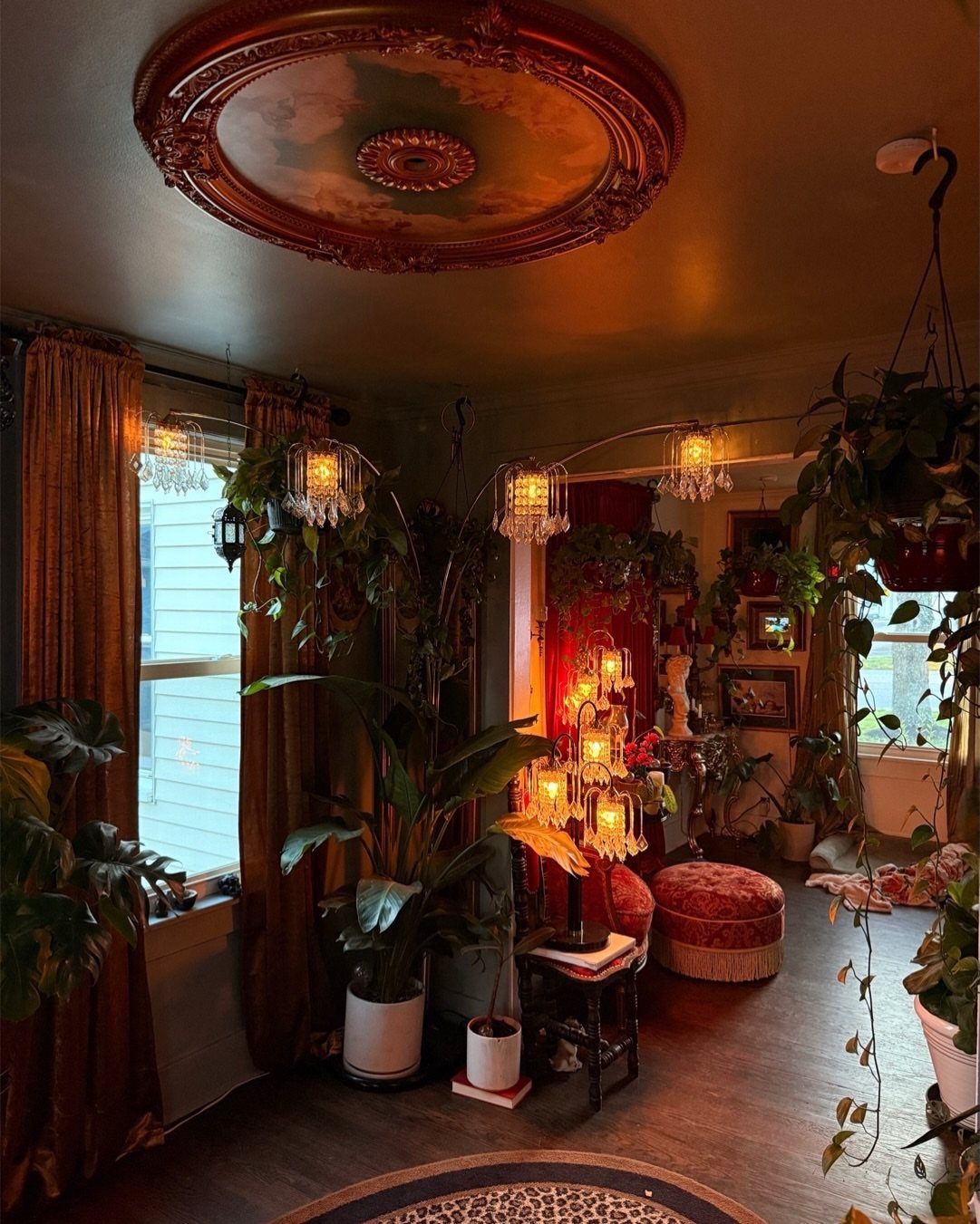 Dark boho living room with lush houseplants, gold curtains, and warm crystal lighting.