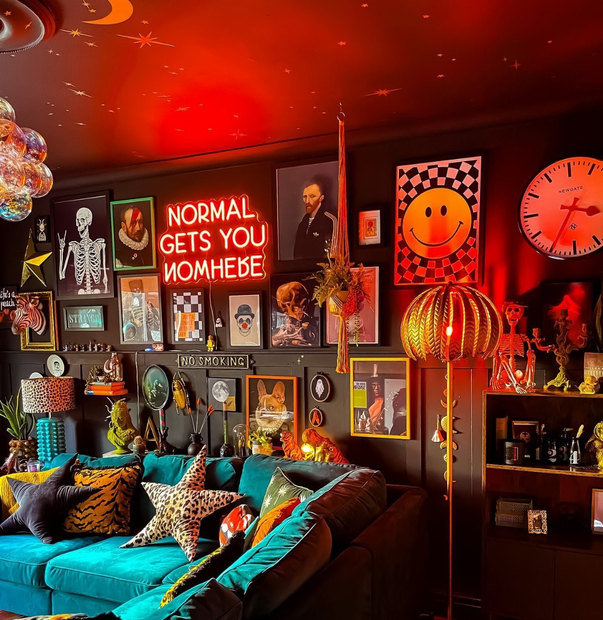 Teal velvet sofa in a dark room with red lighting and eclectic vintage art.