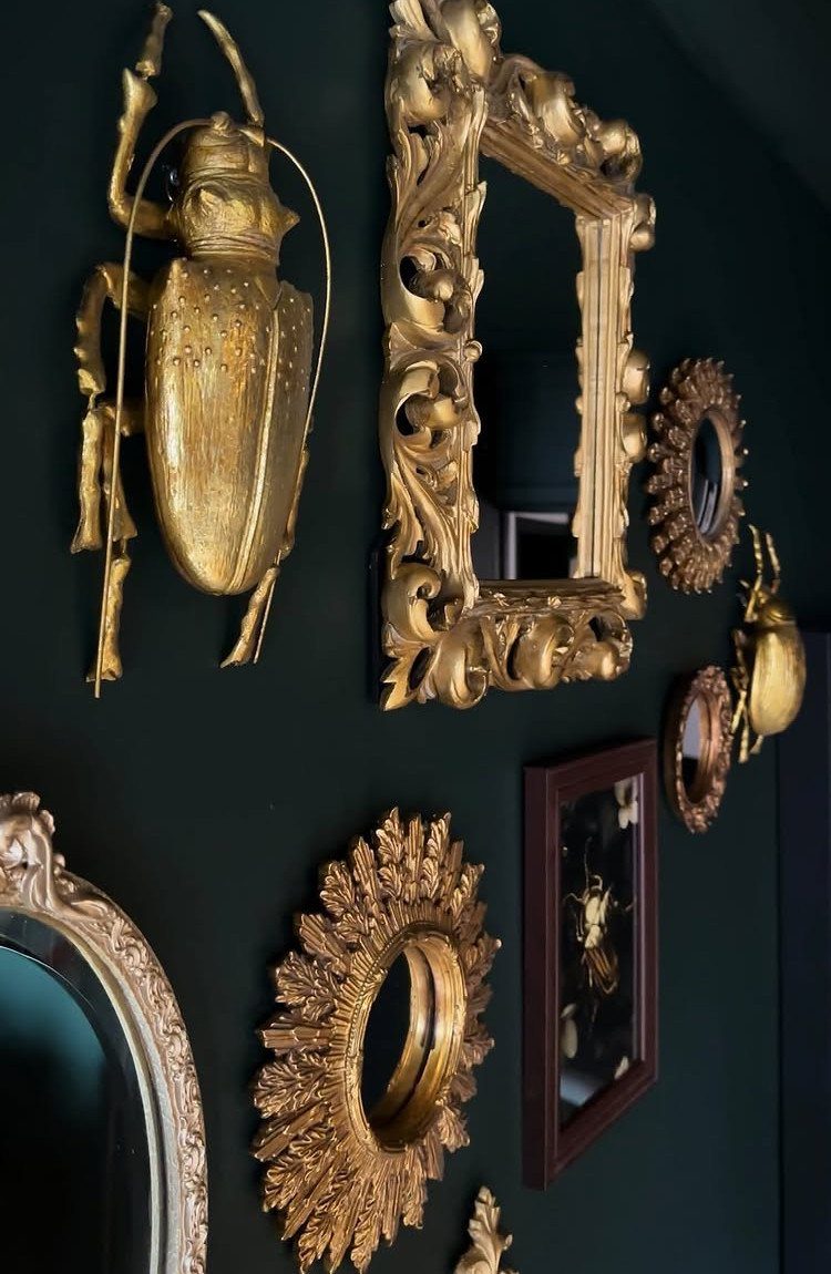 Ornate gold vintage mirrors and a golden beetle sculpture on a dark green wall.