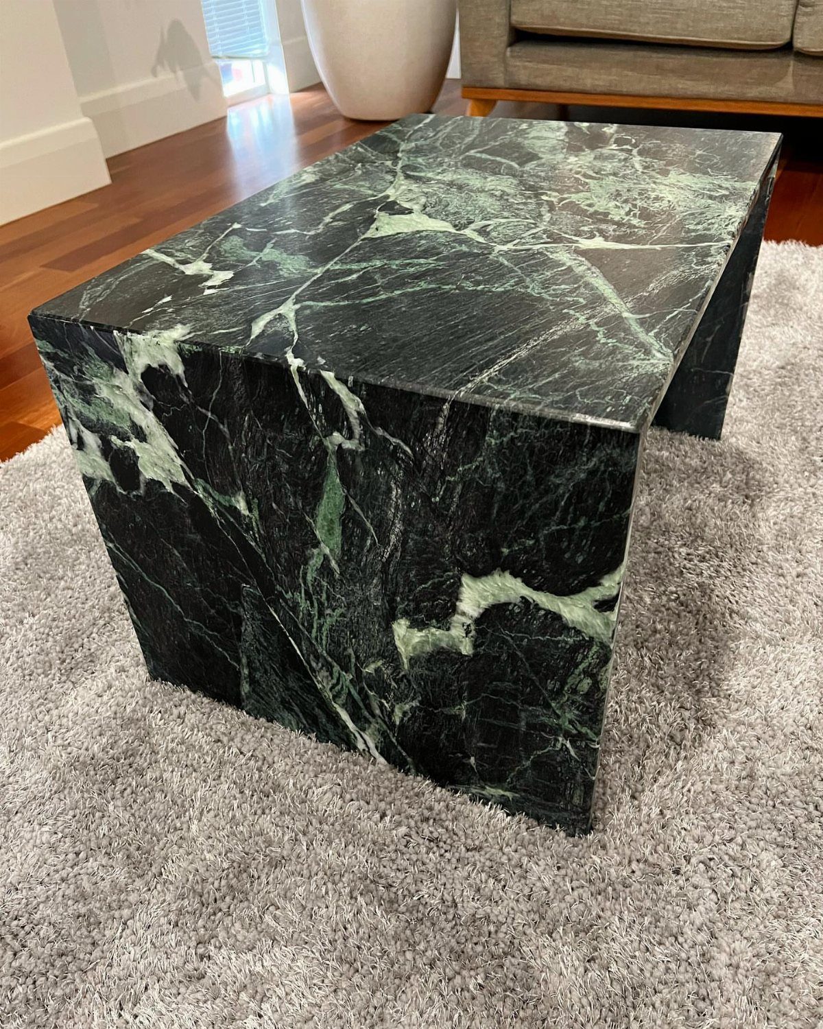 Dark green marble coffee table with white veins on a grey shag rug.