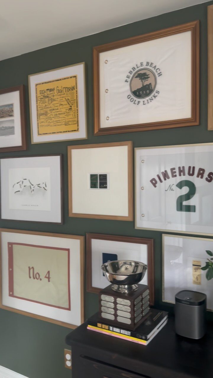 Gallery wall of framed art and documents on a dark green painted wall.