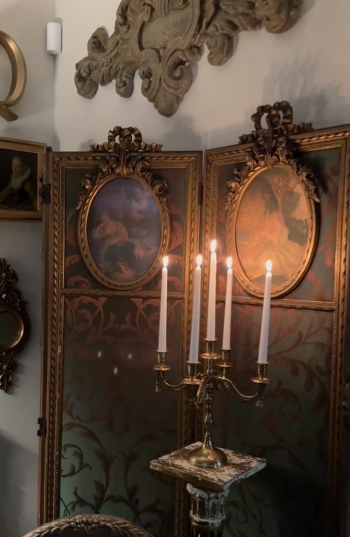 Gold candelabra with lit candles in front of a dark green ornate screen.