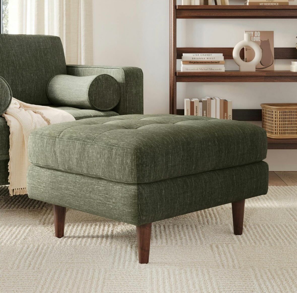 Dark green tufted ottoman with wooden legs in a mid-century modern living room.