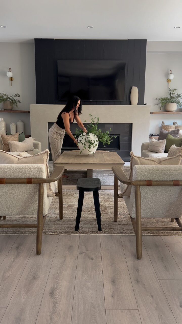 Woman arranging flowers in a living room with beige textured armchairs and dark walls