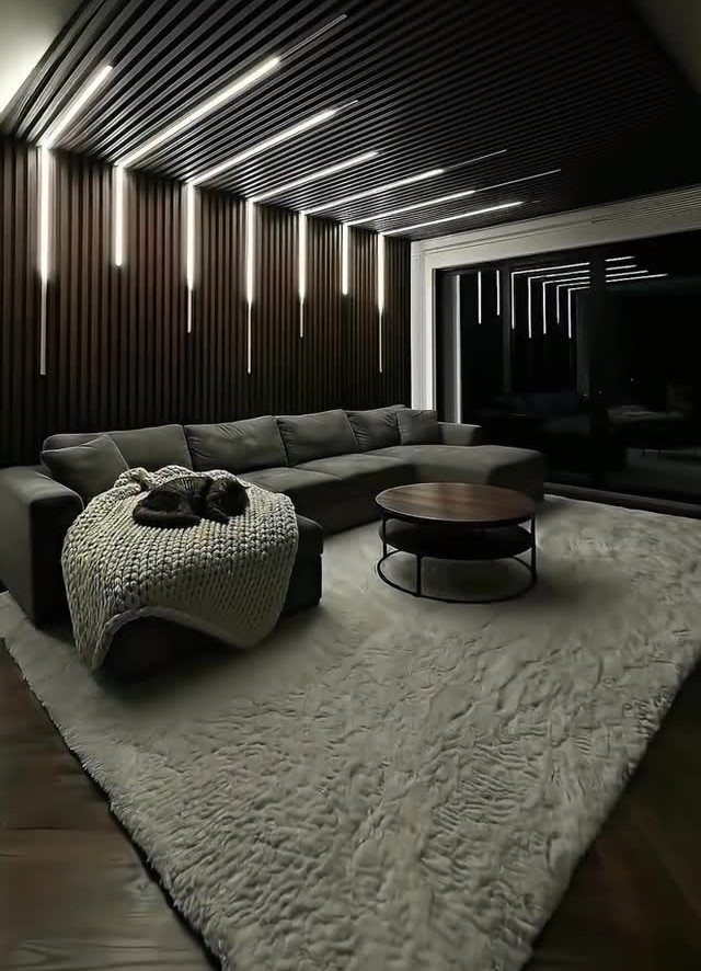 Modern dark living room with slatted wood walls, grey sectional, and linear lighting.