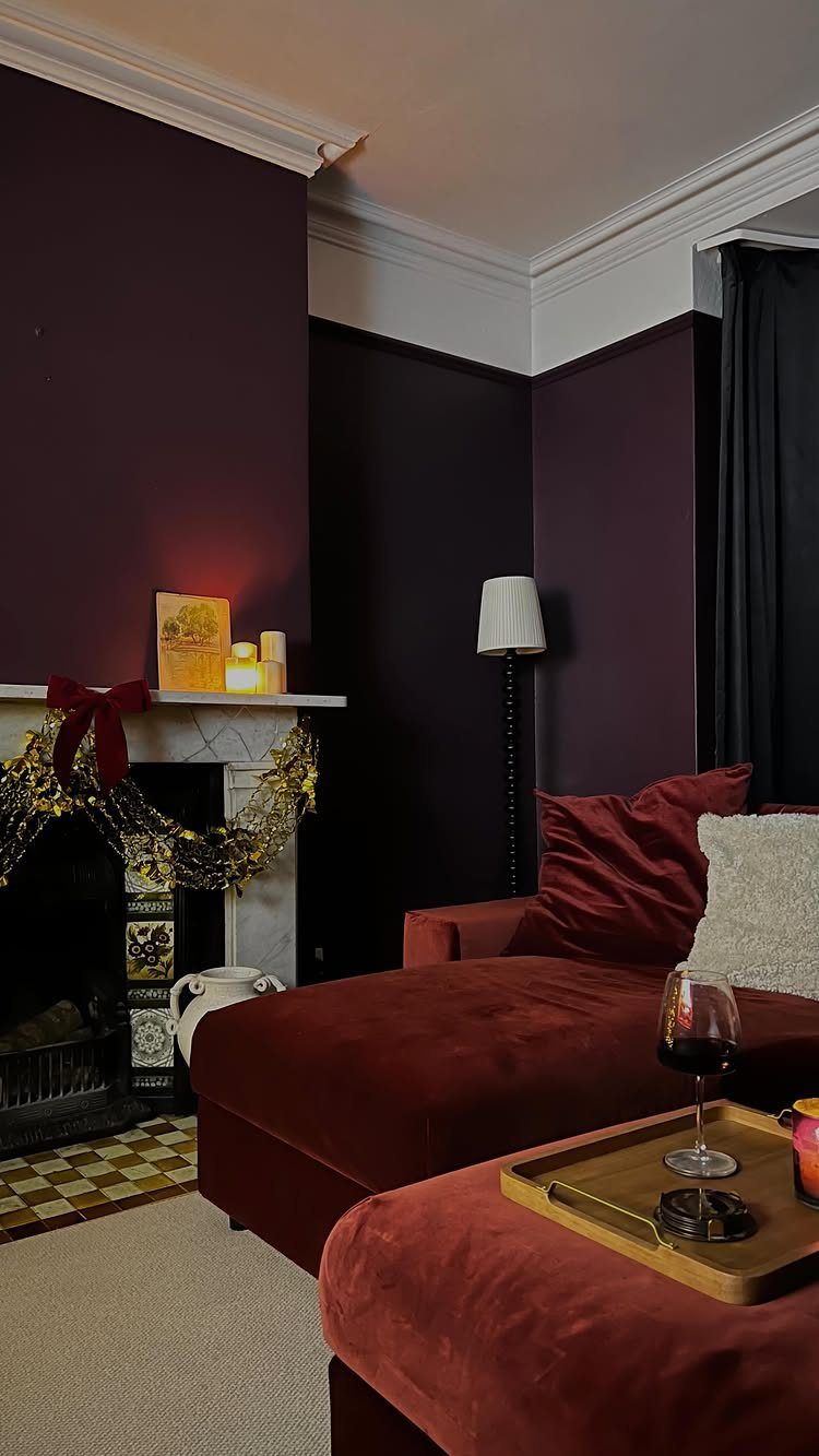 Plum colored living room with red velvet sofa and decorated white fireplace.