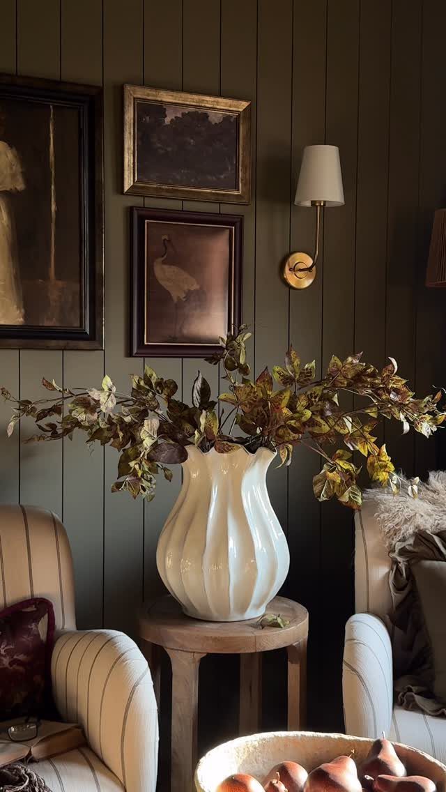 Dark olive green paneled living room wall with framed art and a white fluted vase.
