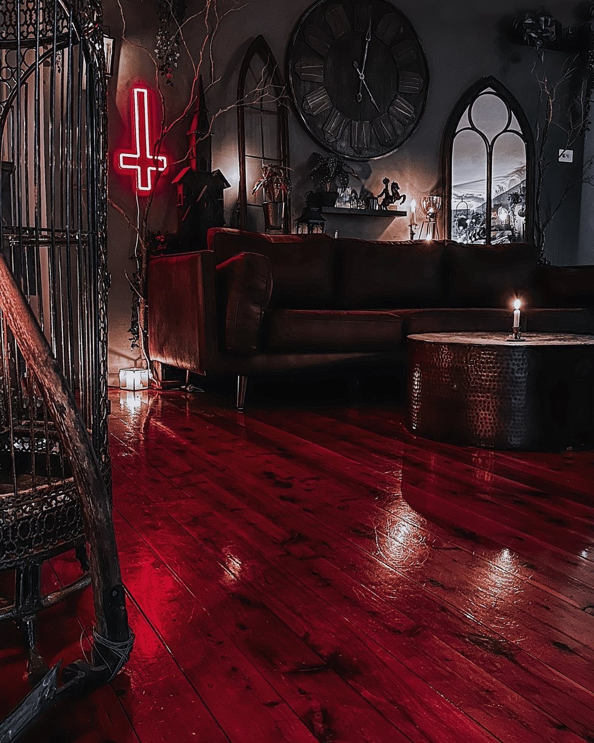 Dark living room with red floors, gothic arch windows, and a red neon cross.