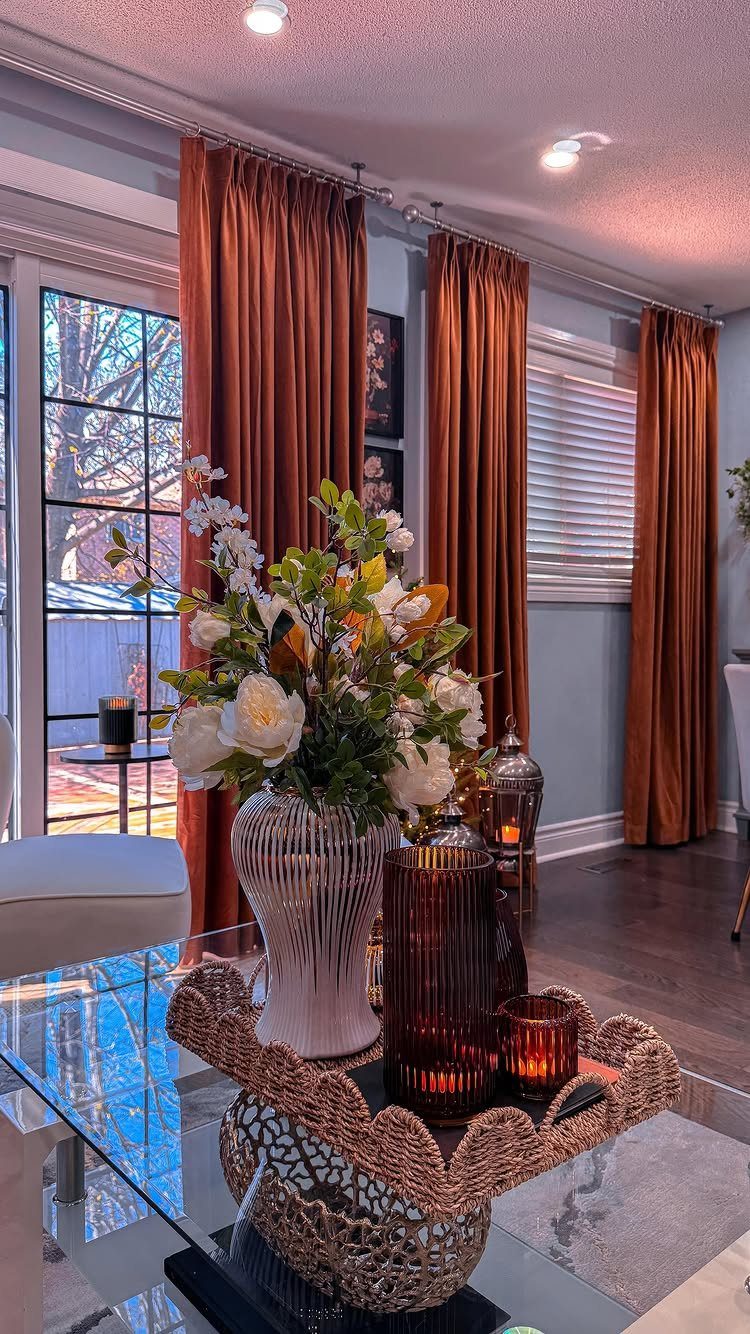 Burnt orange heavy drapes in a living room with white floral arrangement.