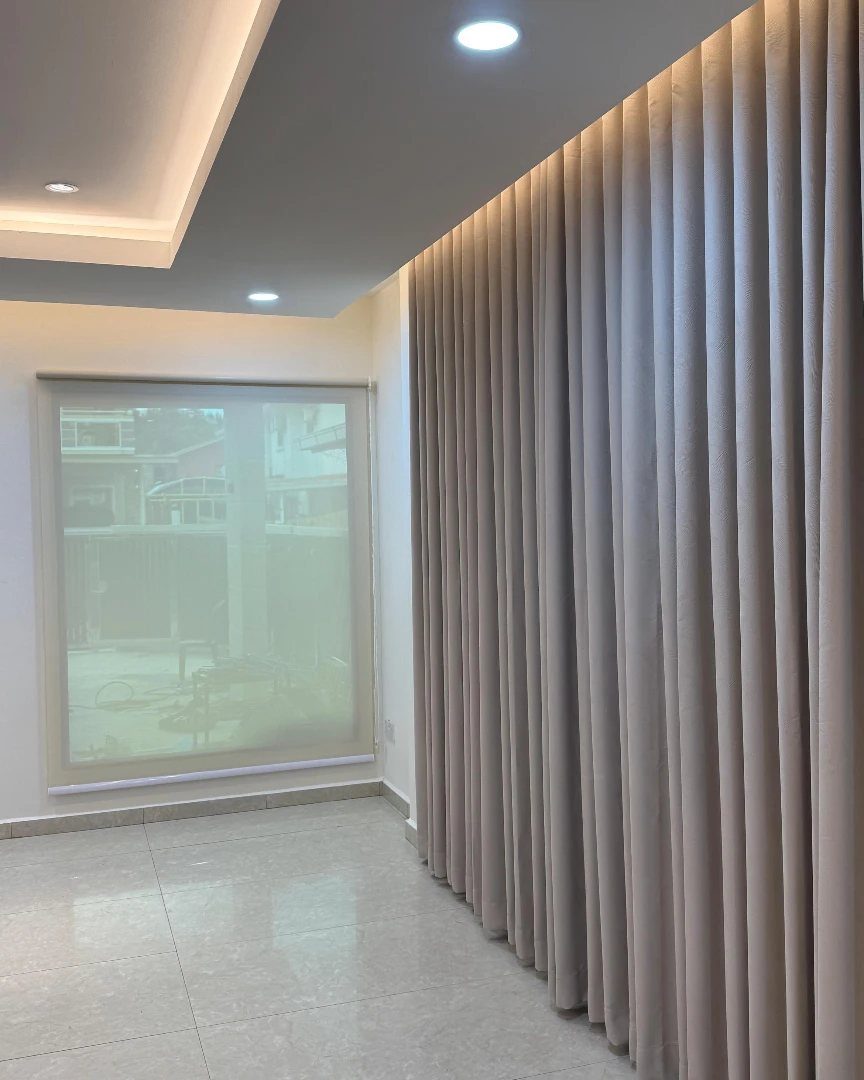 Beige pleated drapery panels hanging from a concealed ceiling track in a modern room.