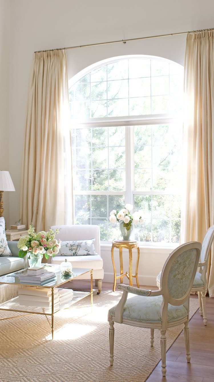 Cream pinch-pleat drapery panels framing a large arched window in a bright living room.