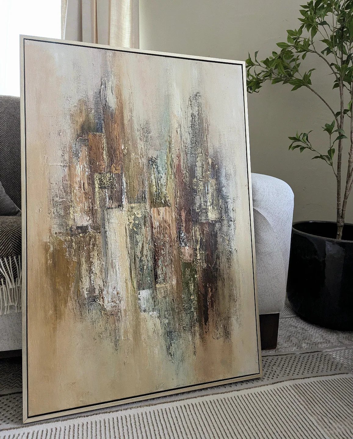 Abstract painting with brown and beige tones leaning against a neutral living room wall.