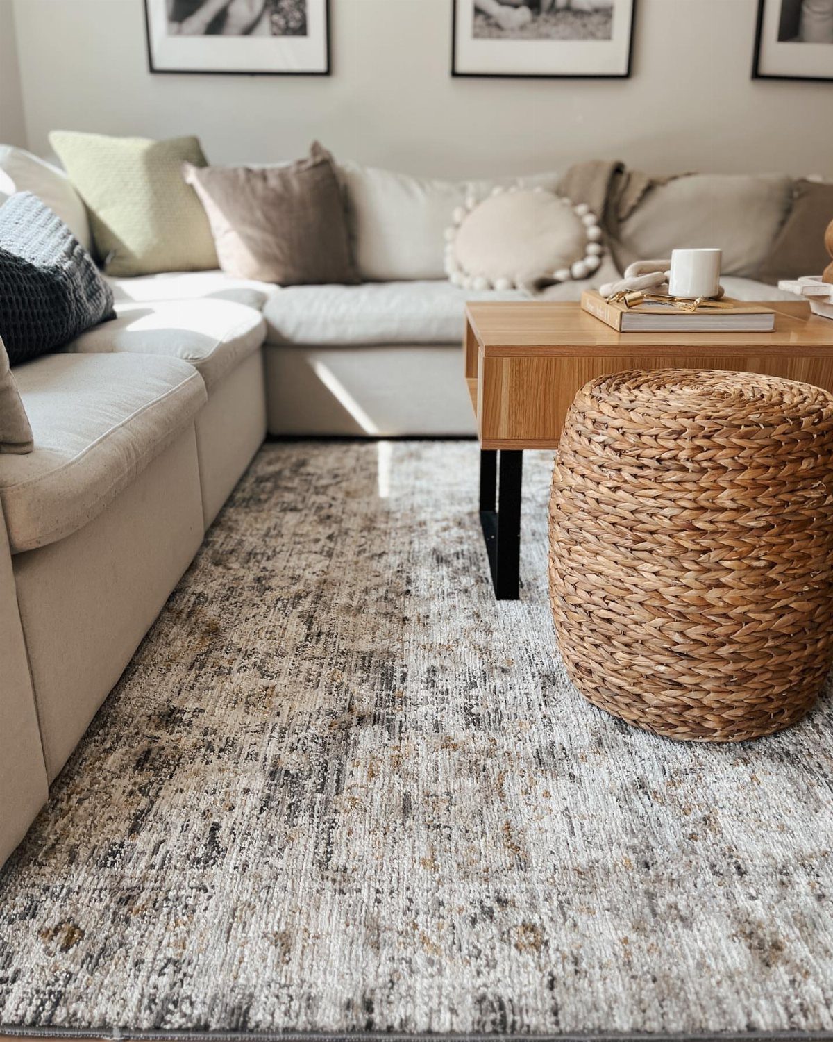 Beige sectional sofa with earth-toned pillows, wooden table, and woven jute pouf.