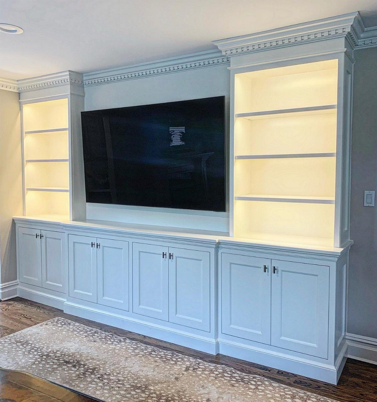 White built-in entertainment center with television, lighted shelves, and storage cabinets below.