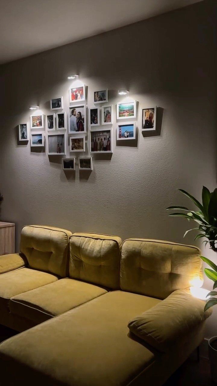 Yellow tufted sofa below a gallery wall of framed family photos with spotlights.