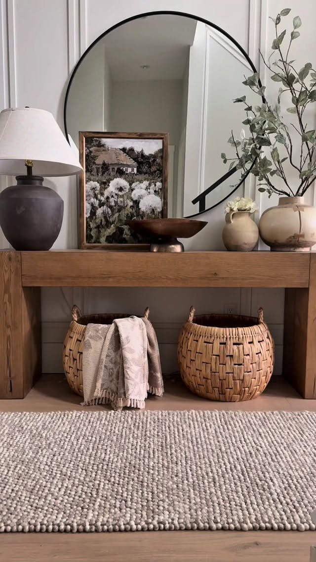 Wooden console table with a round mirror and textured beige rug on the floor.
