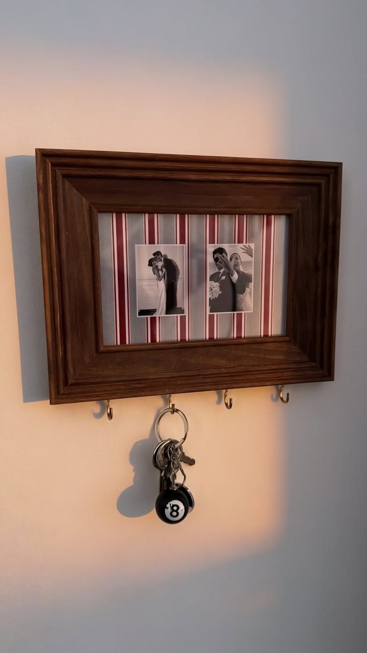 Wooden wall frame with personal photos and key hooks on a white wall.