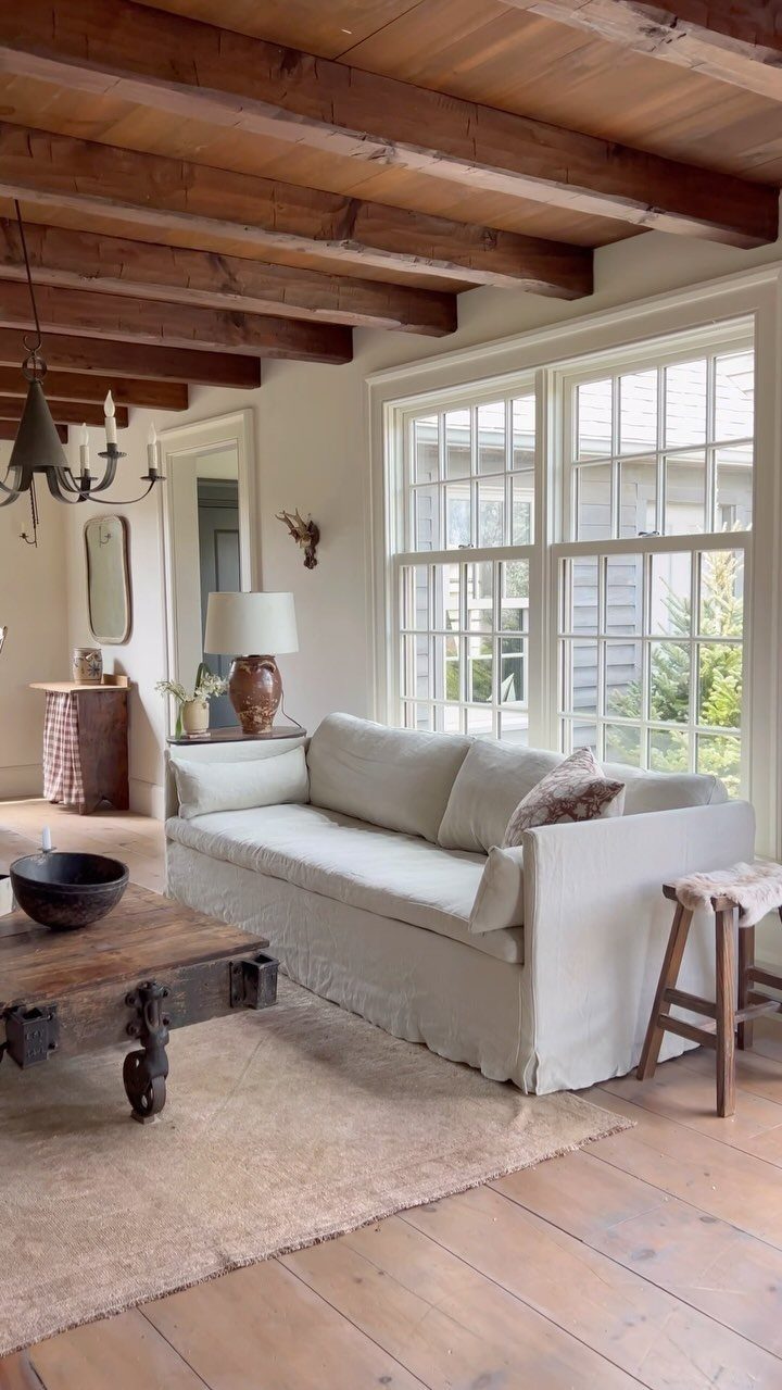 White slipcovered sofa in a farmhouse living room with exposed wooden ceiling beams.
