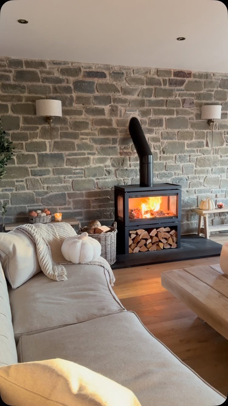 Cozy farmhouse living room with grey stone wall, beige sofa, and black wood stove.