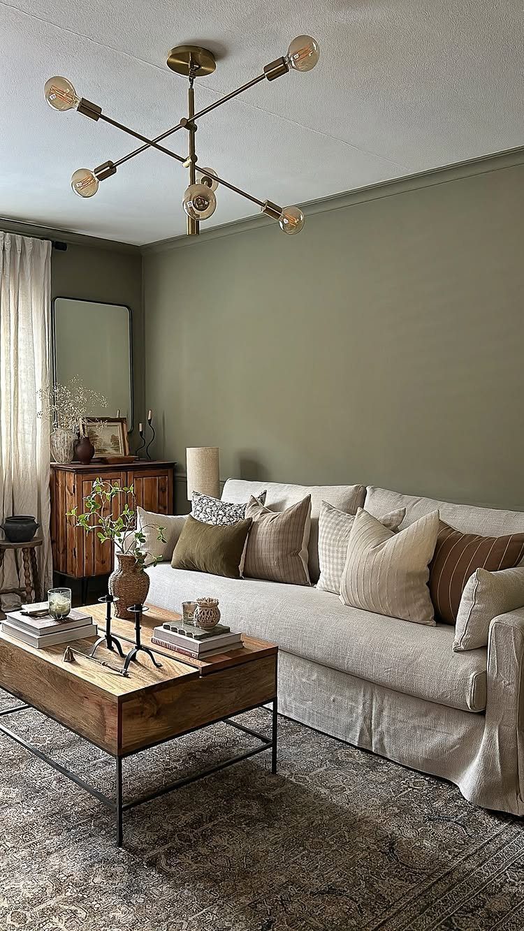 Sage green living room walls with a beige sofa and gold sputnik chandelier.