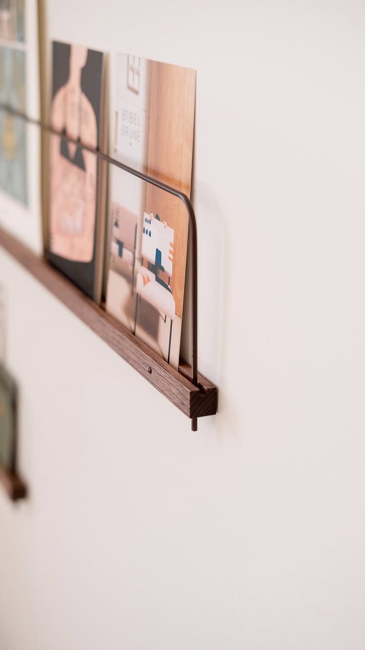 Dark wood floating picture ledge on white wall holding various art prints