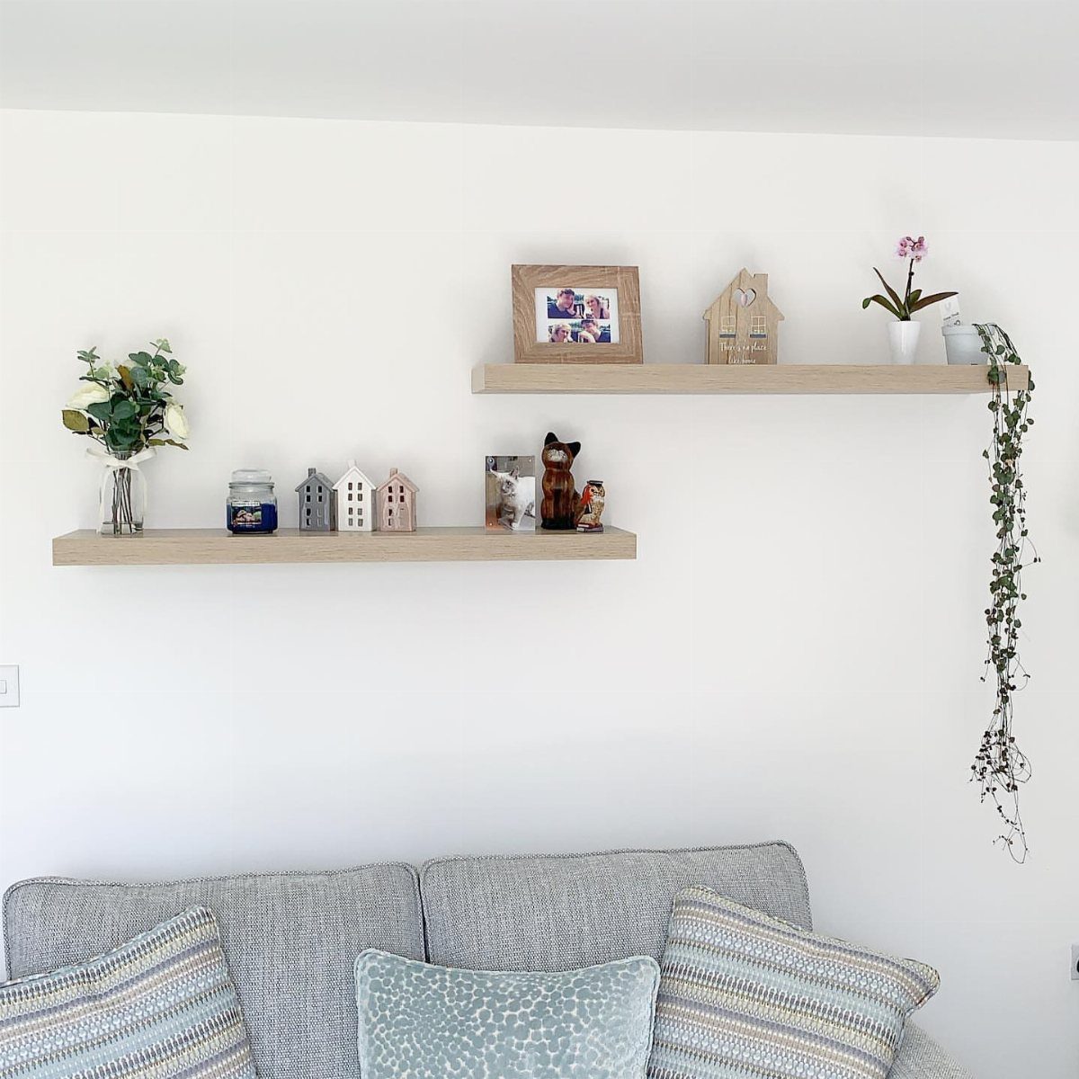 Two light wood floating shelves with decor on a white wall above a sofa
